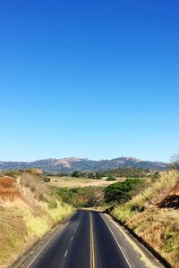 Empty road amidst landscape against clear blue sky