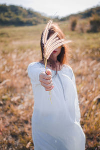 Young woman holding plant against face while standing on field