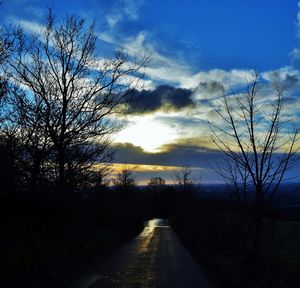 Road amidst bare trees against sky during sunset