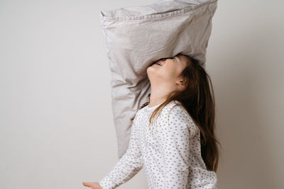 Portrait of pretty caucasian girl in white pyjama and pillow in studio white background