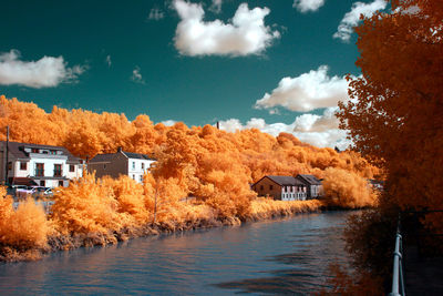 River amidst buildings and trees against sky during autumn