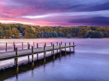 Wooden posts in lake against sky at sunset