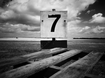 Close-up of information sign by sea against sky