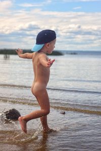 Full length of naked boy wading in sea against sky