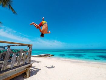 Rear view of man jumping on beach against blue sky