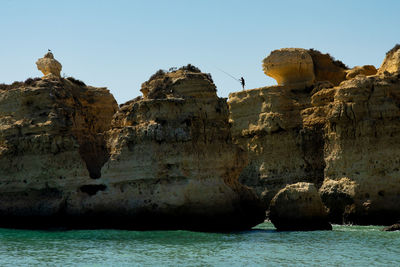 Rock formations by sea against clear sky