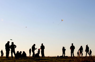 Silhouette people flying kite on field against clear sky during sunny day