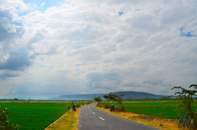 Empty road amidst field against sky