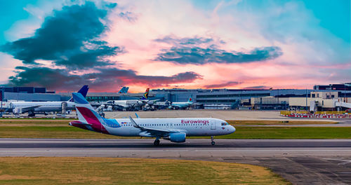 Airplane on airport runway against sky during sunset