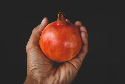 Close-up of hand holding apple against black background