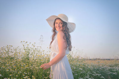 Portrait of young woman wearing hat while standing by plants against sky