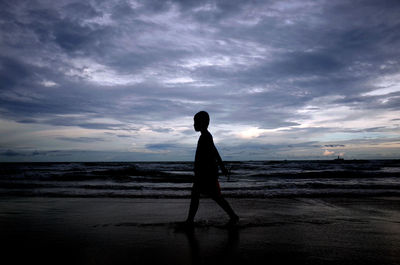 Silhouette man walking on beach against sky during sunset