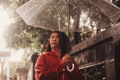 Woman carrying umbrella while standing by retaining wall during monsoon