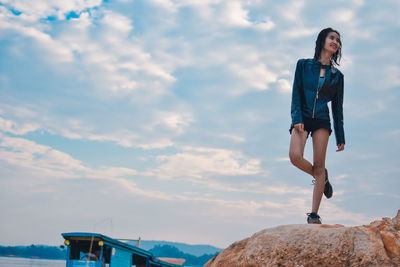 Young woman standing on rock against sky