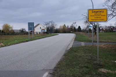 Road sign by trees against sky