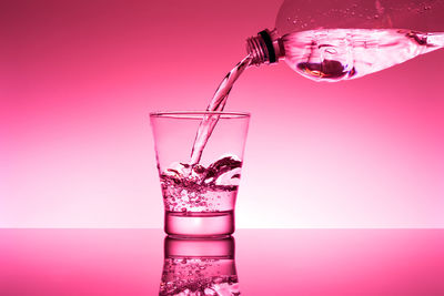Close-up of glass pouring water against pink background