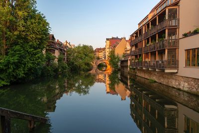 Reflection of buildings and trees in canal against sky