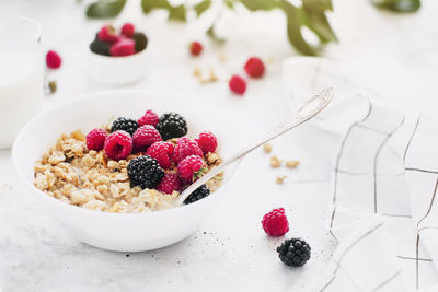 Morning healthy breakfast, white bowl full with granola, muesli, raspberry, blackberry on gray table