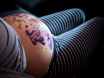 Midsection of pregnant mid adult woman with body paint on belly in darkroom