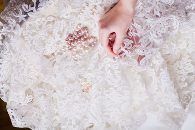 Cropped hand of woman stitching pearls on white wedding dress