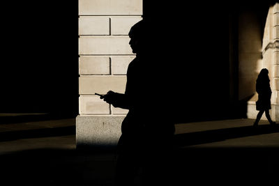 Silhouette man walking on footpath against building