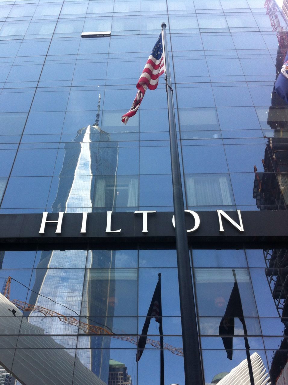 flag, architecture, building exterior, patriotism, national flag, built structure, low angle view, american flag, identity, modern, city, reflection, glass - material, office building, culture, day, skyscraper, building, outdoors, tall - high