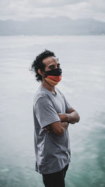 Young man wearing mask standing against sea