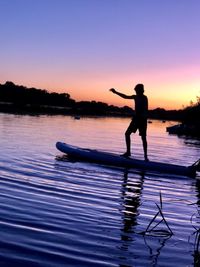 Silhouette boy standing on paddleboard during sunset