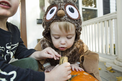 Toddler boy dressed up as an owl closely inspects halloween pumpkin