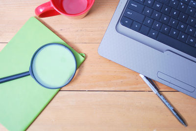 Directly above shot of magnifying glass with laptop and empty mug on desk