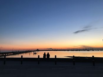 Silhouette people standing against sea during sunset