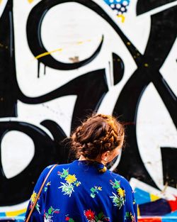 Rear view of woman standing towards graffiti wall