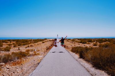 Rear view of woman on road against clear blue sky