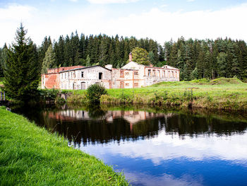 Reflection of house and trees by lake against sky