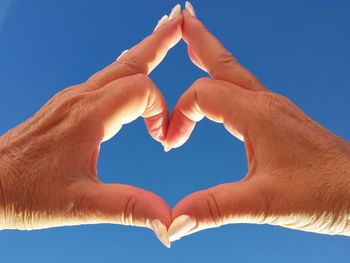 Cropped image of hands forming heart shape against clear sky