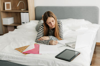 Young woman using digital tablet while sitting on bed at home