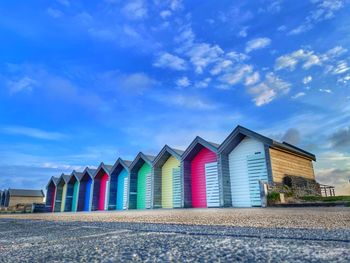 Beach huts by buildings against blue sky