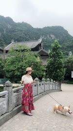 Full length of young woman standing with dog on footbridge 