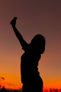 Silhouette man with arms raised against sky during sunset