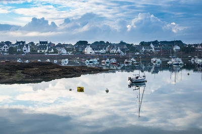 Sailboats moored on harbor by buildings against sky