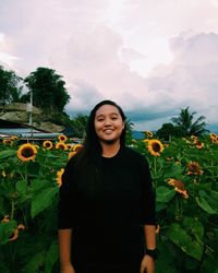 Portrait of smiling woman standing amidst sunflowers on field against sky