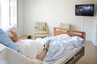 Senior man watching tv while reclining on bed in hospital ward