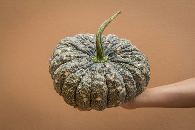 Close-up of hand holding pumpkin against orange background