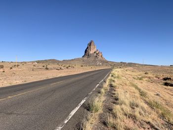 Road amidst desert against clear blue sky