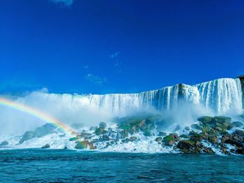 Scenic view of rainbow over sea against blue sky