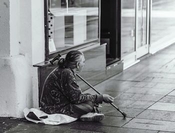 Man sitting on footpath by window