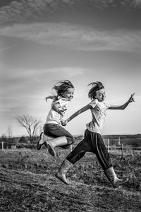 Full length of two  young girls standing on field against sky.