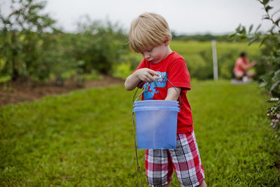 Boy holding bucket while standing on grassy field at park