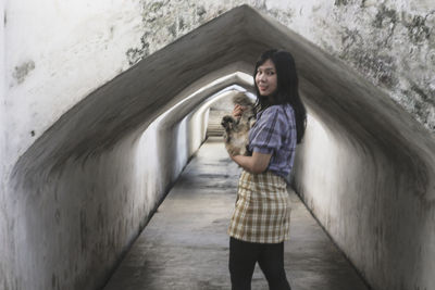 Portrait of smiling young woman standing against wall