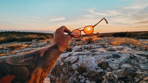 Hand on rock against sky during sunset